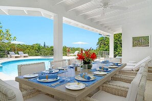 A dining area with a pool view, white furniture, and a ceiling fan. - Tranquil 4BR Villa Pool Spa Resort Access (Montego Bay)
