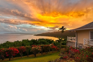 A coastal landscape with a sunset, lush greenery, and a house with a stone wall and white gate. - Private 2BR Open-air Villa Panoramic Views Pool (Montego Bay)