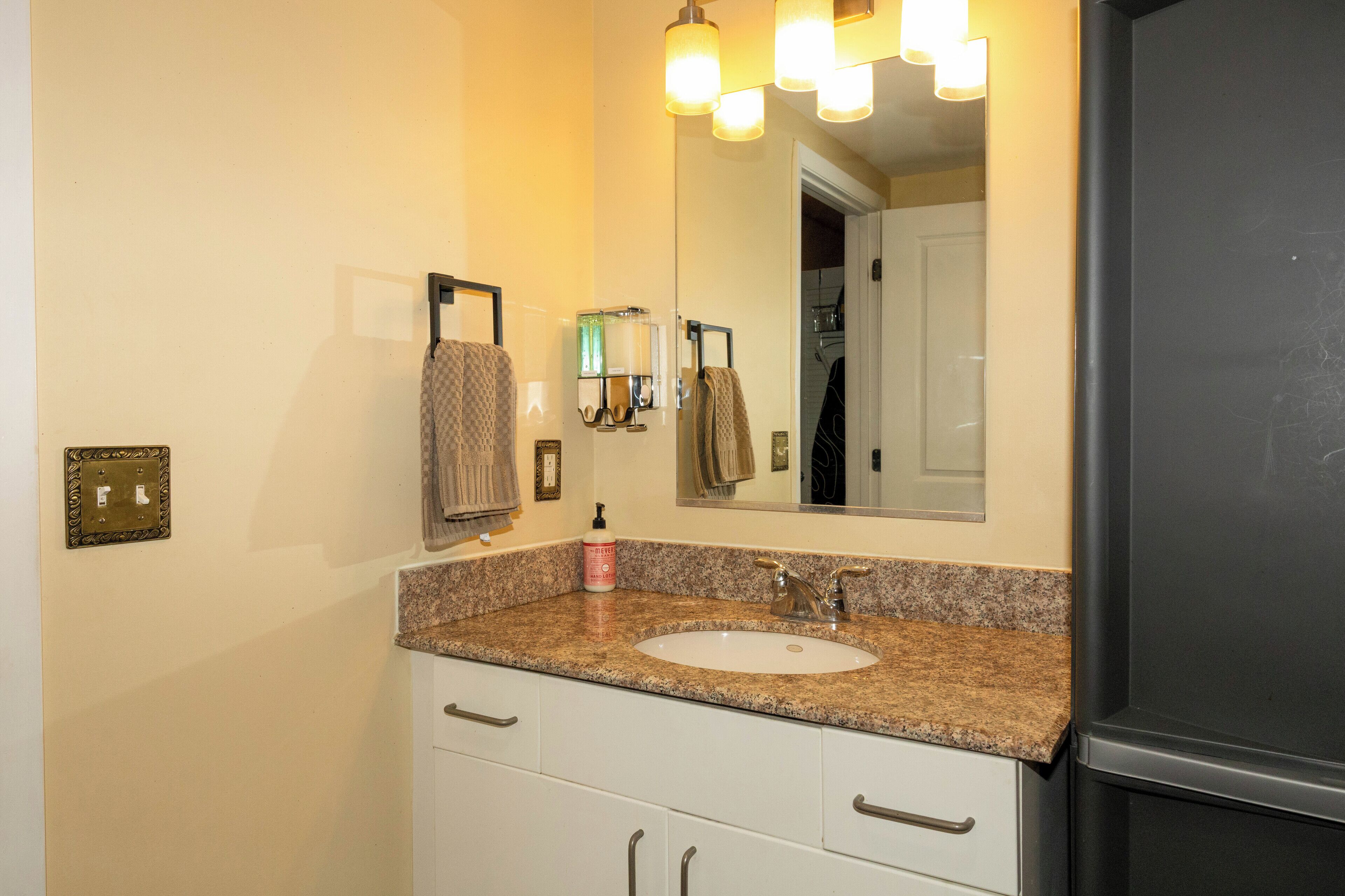 A bathroom with a granite countertop sink, a mirror, a towel rack, and a door leading to another room.