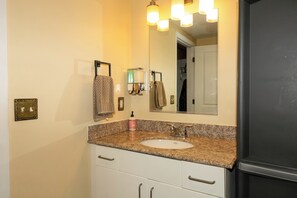A bathroom with a granite countertop sink, a mirror, a towel rack, and a door leading to another room. - Fair and Walker (Atlanta)