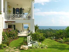 A two-story building with a balcony, a garden with a pathway, and a view of the sea.