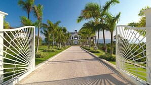 A gated entrance to a property with a paved driveway, palm trees, and a view of the ocean. - Expansive 6BR Estate Panoramic Sea Views Pool Resort Access (Montego Bay)