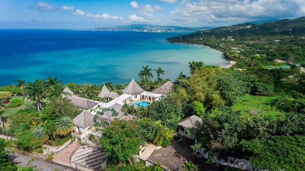 Un resort con varias construcciones de techo de paja, una piscina y abundante follaje.