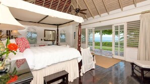 Un dormitorio amplio con una cama grande, un ventilador de techo y vista al océano a través de un ventanal corredizo.
