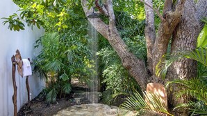 A stone pathway leading to a small waterfall in a lush garden with a wooden chair and a white wall. - Nature-inspired 4BR Modern Villa Pool Resort Access (Montego Bay)
