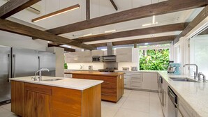 A modern kitchen with wooden cabinetry, stainless steel appliances, and a large island. - Nature-inspired 4BR Modern Villa Pool Resort Access (Montego Bay)