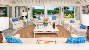 A spacious living room with a view of a pool and lush greenery. - Private 4BR Open-air Villa Panoramic Views Pool (Montego Bay)
