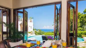 Une table à manger avec des aliments pour le petit-déjeuner, donnant sur une piscine et l’océan.