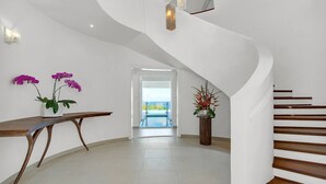 A modern interior with a curved staircase, a wooden bench, and two potted plants. - Contemporary 6BR Villa Sea Views Infinity Pool Resort Access (Montego Bay)