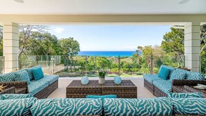 A modern outdoor seating area with wicker furniture and patterned cushions, overlooking a lush landscape and the ocean. - Contemporary 6BR Villa Sea Views Infinity Pool Resort Access (Montego Bay)