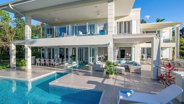 A modern two-story house with a swimming pool, outdoor seating, and a balcony with glass railings. - Contemporary 6BR Villa Sea Views Infinity Pool Resort Access (Montego Bay)
