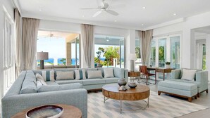 A spacious living room with a large sofa set, a coffee table, and a view of the outdoors. - Contemporary 6BR Villa Sea Views Infinity Pool Resort Access (Montego Bay)