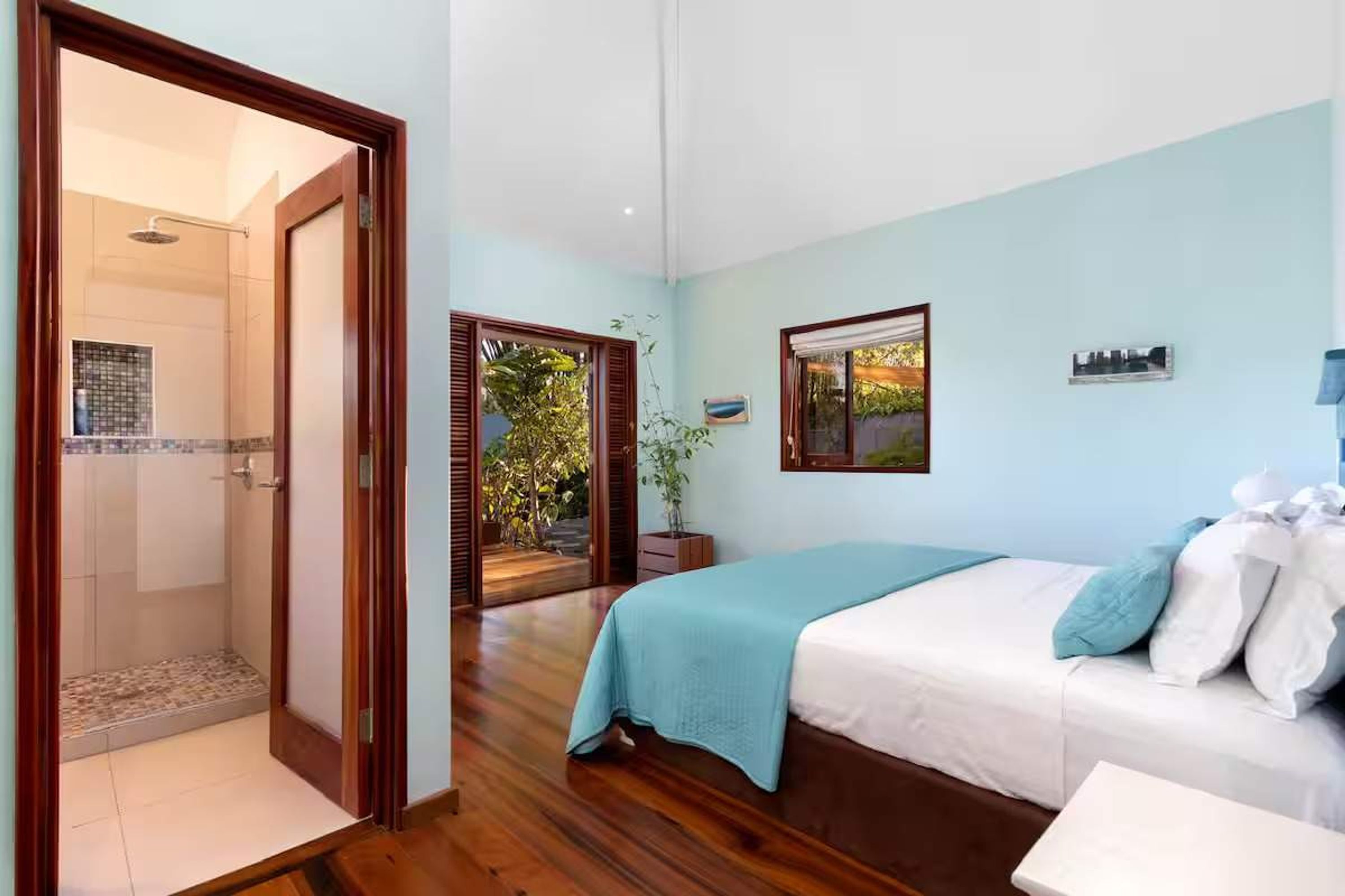 Un dormitorio con cama, mesita de noche, ventana y puerta que da a un baño.