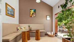 A modern living room with a glass-top coffee table, wooden legs, a beige sofa, and a large window with a view of the outdoors. - Hidden 4BR Gem Pool Nature Escape in the Hills of Port Antonio (Port Antonio)