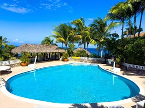 A clear blue pool surrounded by palm trees and a thatched-roof structure, with a view of the ocean. - 4BR Seafront Villa in Boscobel Direct Sea Access Coastal Living (Boscobel)