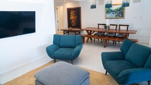 A modern living room with teal armchairs, a wooden dining table, and a large painting on the wall. - 4BR Seafront Villa in Boscobel Direct Sea Access Coastal Living (Boscobel)