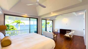 A spacious bedroom with a large bed, a ceiling fan, and a view of the ocean through large windows.