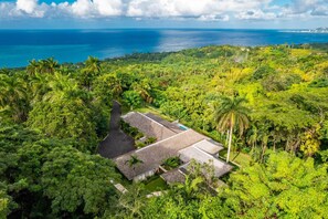 A tropical resort with multiple bungalow-style buildings surrounded by dense greenery and a view of the ocean. - Secluded 3BR Garden Villa Pool Ocean Views (Sandy Bay)