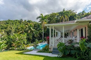 A covered outdoor seating area with a pool, surrounded by lush tropical vegetation. - Secluded 3BR Garden Villa Pool Ocean Views (Sandy Bay)