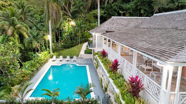 A pool with a white deck, surrounded by lush greenery and a white building with a tiled roof. - Secluded 3BR Garden Villa Pool Ocean Views (Sandy Bay)