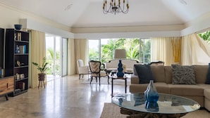 A spacious living room with a glass coffee table, a sofa, and a bookshelf. - Secluded 3BR Garden Villa Pool Ocean Views (Sandy Bay)
