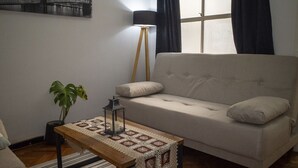 En stue med sofa, sofabord i træ, gulvlampe og en potteplante.