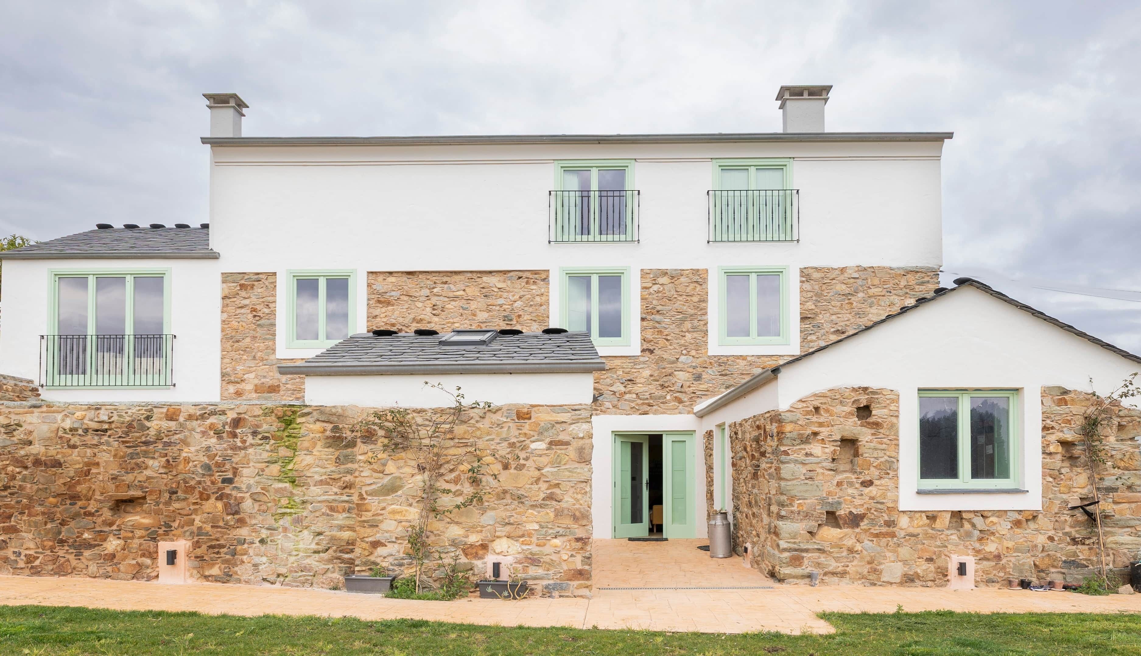 A two-story stone house with green shutters, a small balcony, and a stone wall entrance.