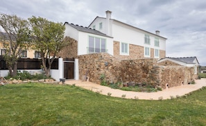 Una casa de dos pisos con fachada de piedra, terraza de madera y un patio cubierto de césped.