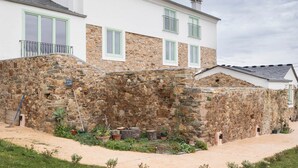 Une maison en pierre à deux étages, avec une façade blanche, des volets verts et un mur en pierre.