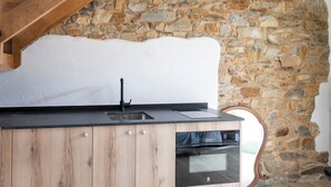 Uma cozinha com parede de pedra, armários de madeira e bancada preta.