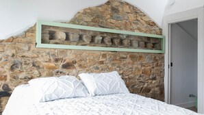 Quarto com parede de pedra, teto de madeira e cama com roupa de cama branca.