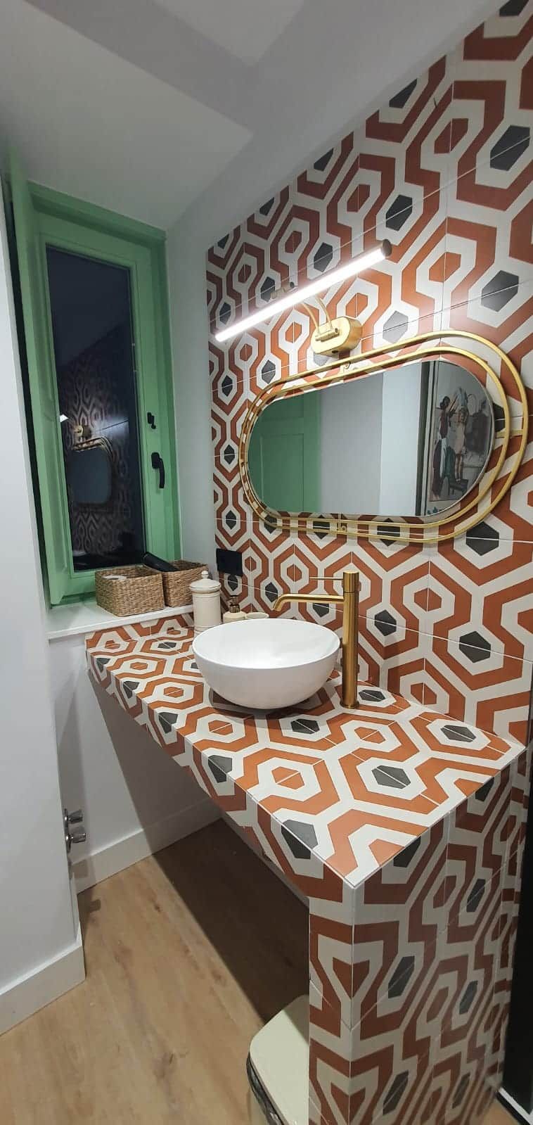 Ein Badezimmer mit einem fugenreichen Fliesenrückwand, einem weißen Waschbecken mit Goldarmatur und einem Spiegel mit goldfarbener Rahmung.