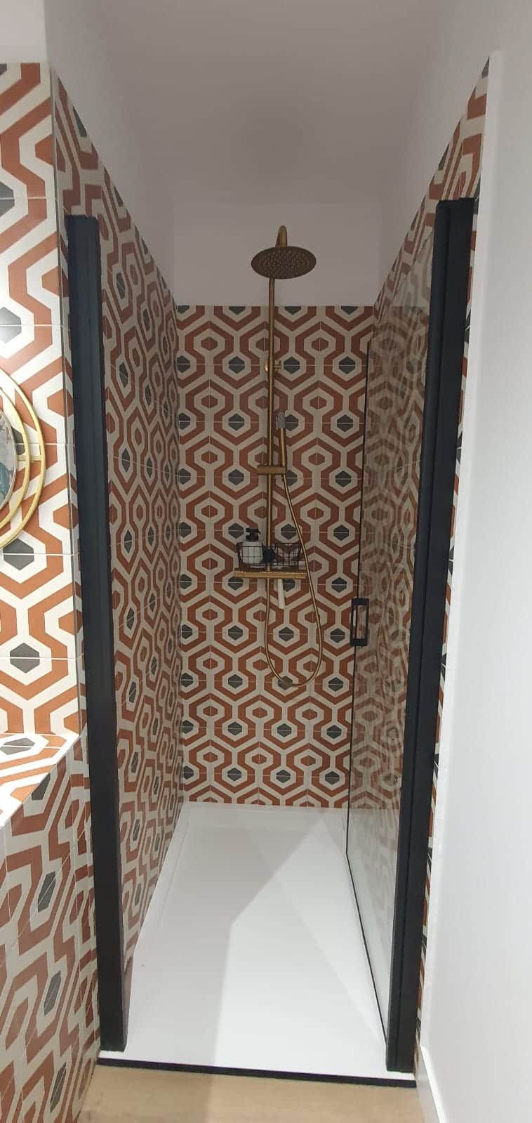 Eine Dusche mit Wandpaneelen in geometrischem Muster, einer Deckenleuchte und einem sichtbaren Bedienfeld.