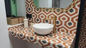 Un baño con pared estampada, un espejo redondo, un lavabo blanco y un pequeño cubo de basura.