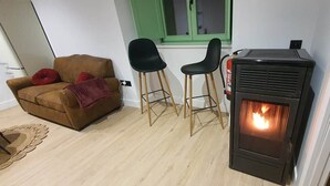 Una sala de estar con un sofá marrón, dos sillas negras, un estufa de leña negra y una ventana con detalles verdes.