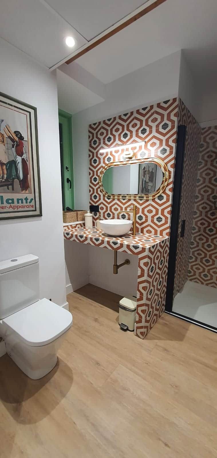 A bathroom with a patterned wall, a toilet, a sink with a mirror, and a trash bin.