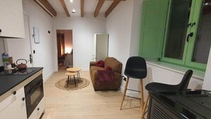 Un espacio habitable compacto con kitchenette, comedor y zona de estar con sofá y sillas.