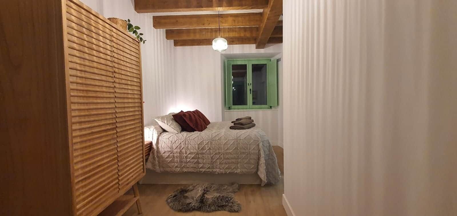 Un dormitorio con cama, un armario de madera, un ventanal verde y una lámpara en el techo.