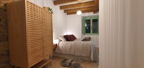 A bedroom with a bed, a wooden wardrobe, a green window, and a hanging light fixture.