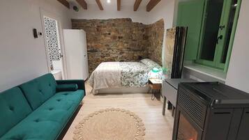 Una habitación pequeña y acogedora con cama, sofá verde, chimenea y pared de piedra.