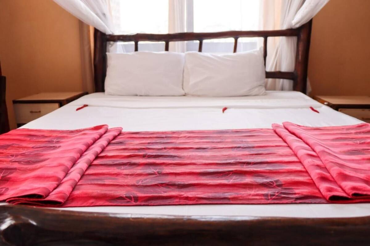 A neatly made bed with white linens and a red patterned blanket, wooden headboard, and two bedside tables.