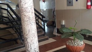 A lobby with a marble staircase, a central pillar, a potted plant, and a fire extinguisher on the wall. - Bridge Hotel Mombasa (Mombasa)