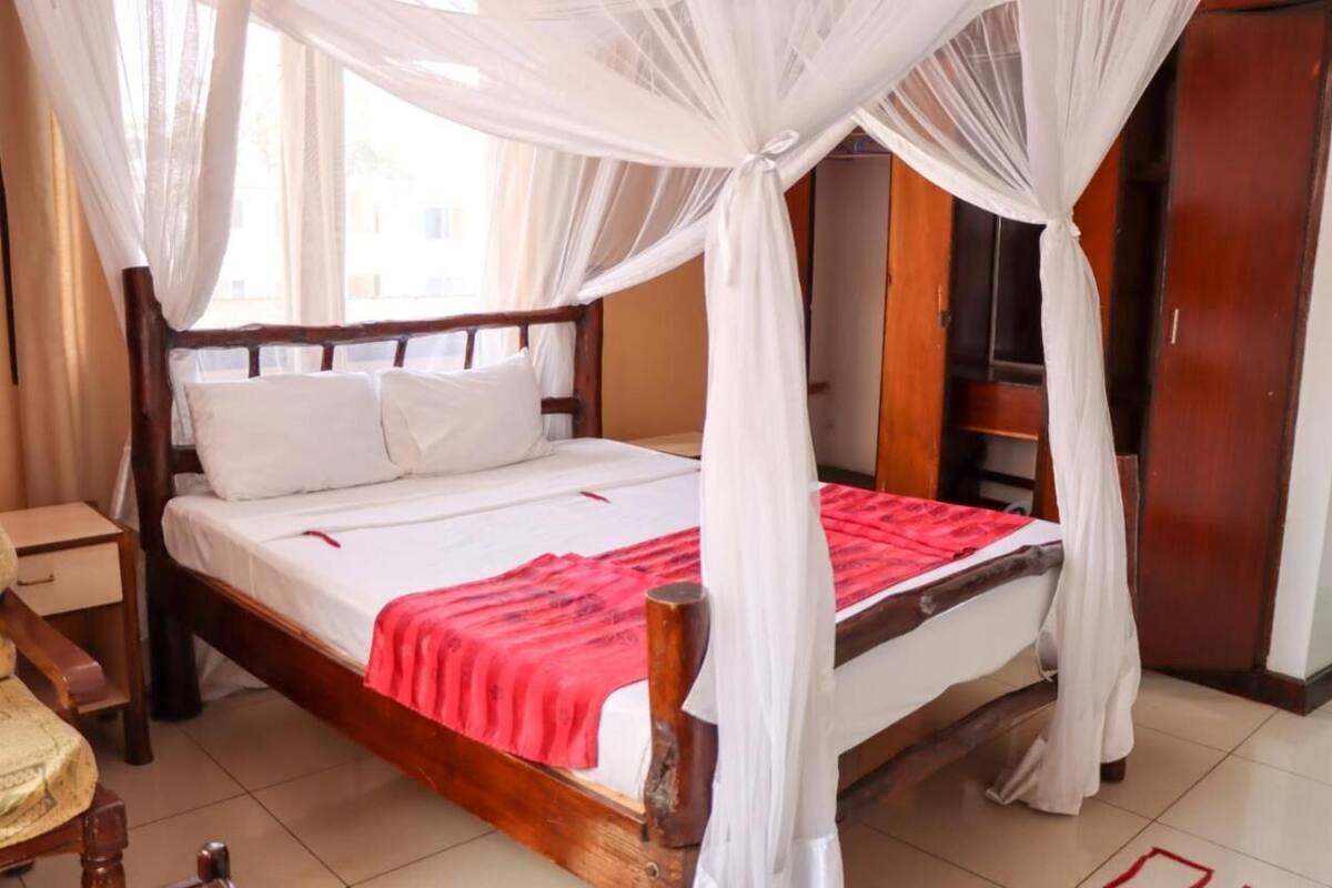 A room with a four-poster bed, white bedding, and a red blanket.