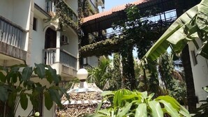 A multi-story building with balconies covered in greenery, a palm tree, and a covered walkway. - Bridge Hotel Mombasa (Mombasa)