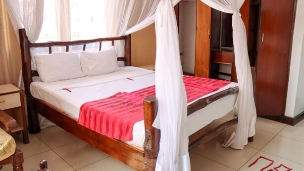 A room with a wooden bed, white bedding, a red blanket, and a canopy. - Bridge Hotel Mombasa (Mombasa)