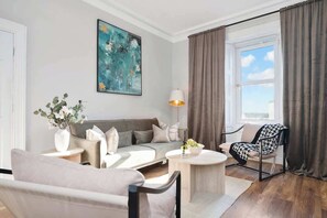 Un salon moderne avec un canapé, des fauteuils, une table basse, une lampe et un tableau accroché au mur.