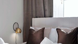 A neatly made bed with white and brown pillows, a gold lamp, and a window with curtains. - Milton Apartment - 3 Beds, Kirkcaldy with sea view (Fife)