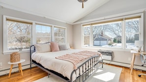 A bedroom with a bed, a radiator, a lamp, and a window with a view of a house and trees.
