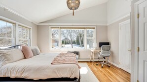 Ein Schlafzimmer mit einem großen Bett, einem Schreibtisch mit Stuhl, einem Fenster mit Blick auf Bäume und einer Chandelier.
