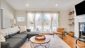 A modern living room with a grey sofa, a round wooden coffee table, and a television mounted on the wall.
